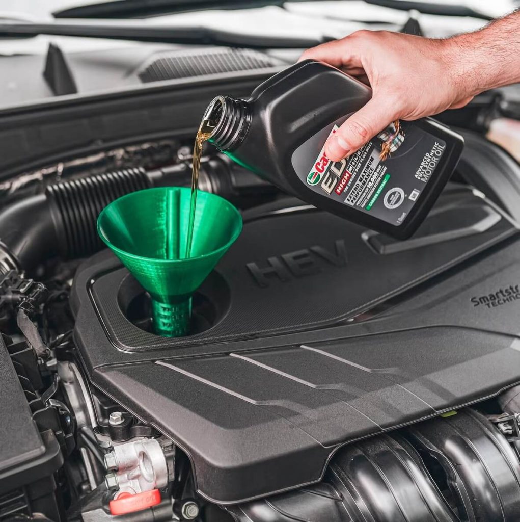 bottle of castrol synthetic oil being poured into a green funnel for an HEV engine
