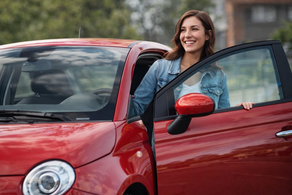 Happy Fiat driver stepping into red Fiat after service at trusted auto repair shop in Grand Haven, MI